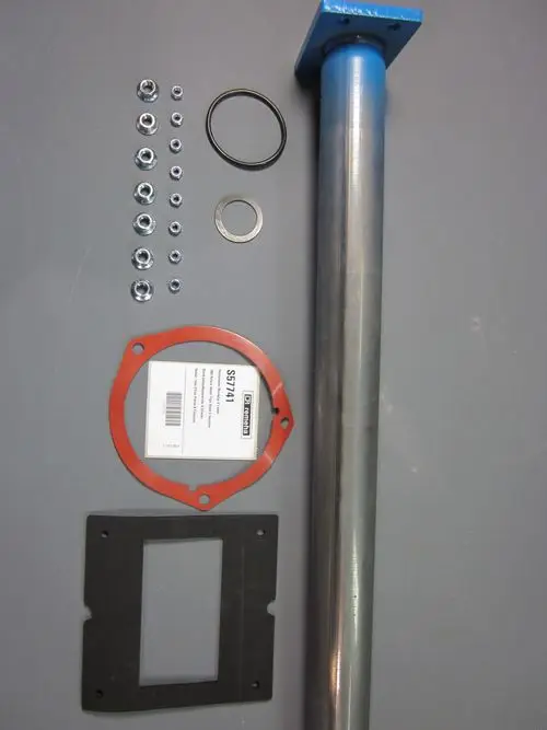 Remeha Zubehörteile, einschließlich eines Metallrohrs, Dichtungen, Unterlegscheiben und Schrauben, auf einem grauen Untergrund angeordnet.